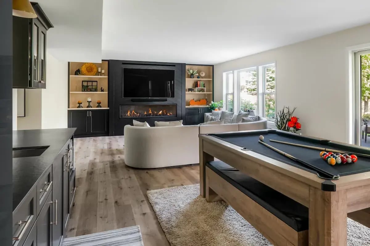 a basement with gaming area, partial kitchen, and built-in fireplace with TV.