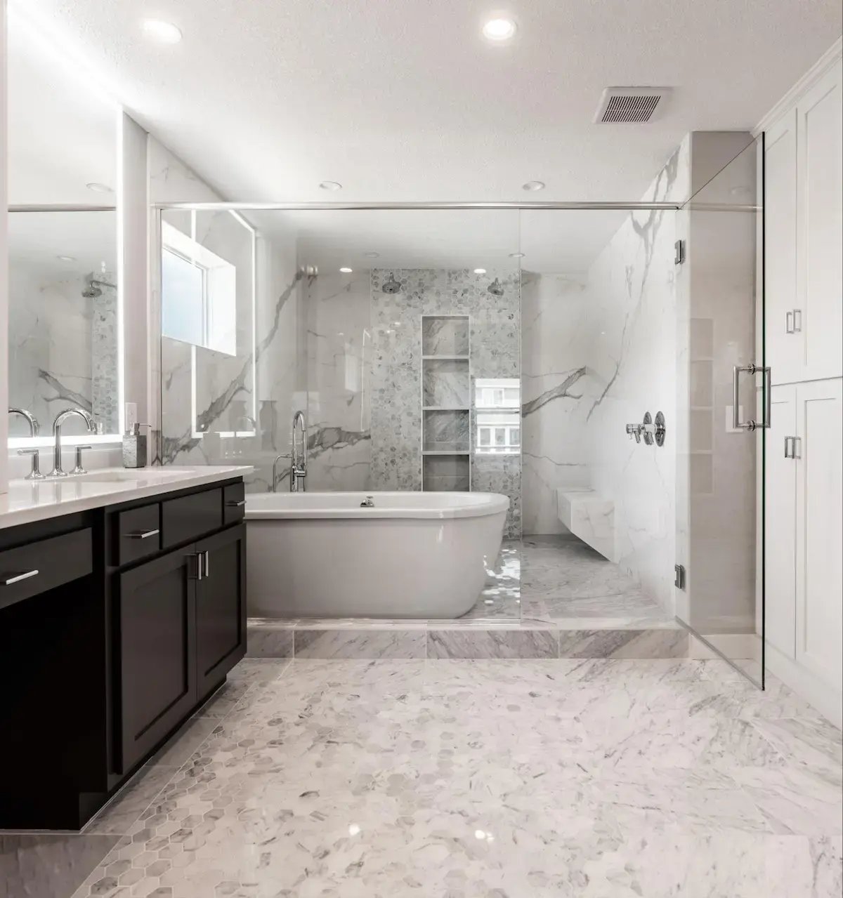 Titus project: modern, luxurious bathroom with a marble tile floor and walls. It features a freestanding bathtub, a large mirror above a sink, and a walk-in shower with a glass door