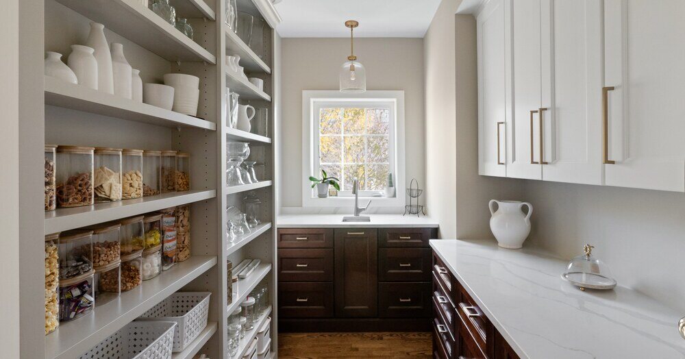 a large pantry with surfaces for preparing food, a sink, and a window.